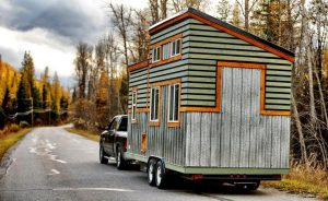 a wooden home on wheel driven by a pick up truck